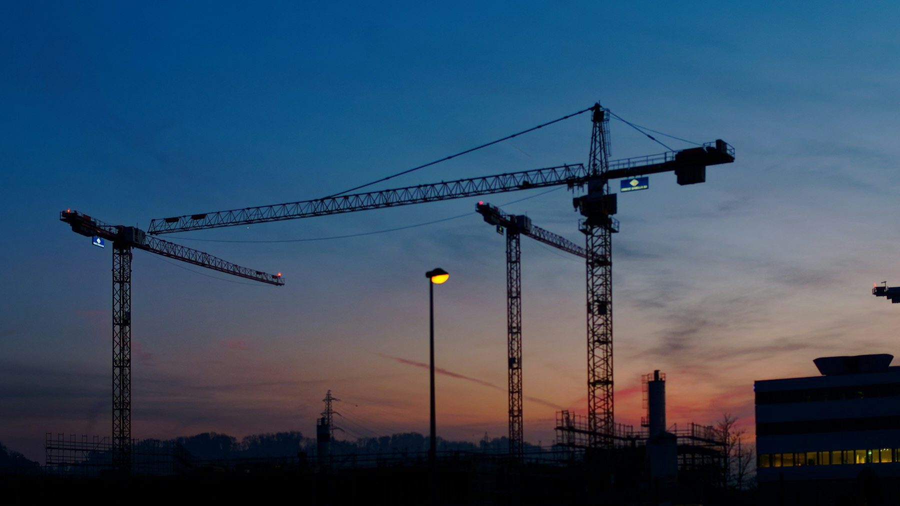 Tower cranes silhouetted against a dusk sky on a construction site