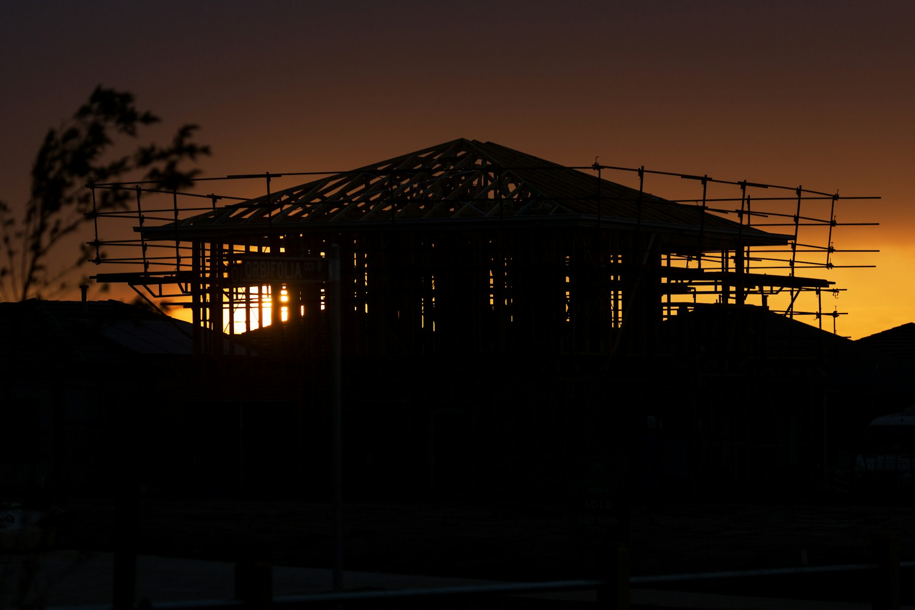 A house frame and scaffolding silhouetted against a sunset